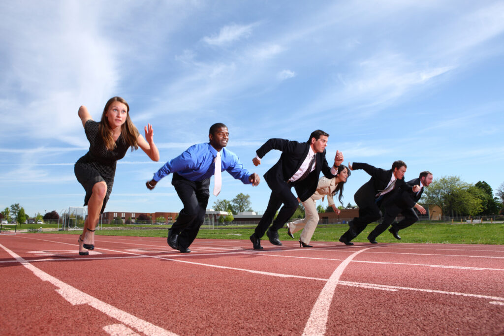 Business professionals in starting positions on a running track, symbolizing competition and hustle culture in the workplace.