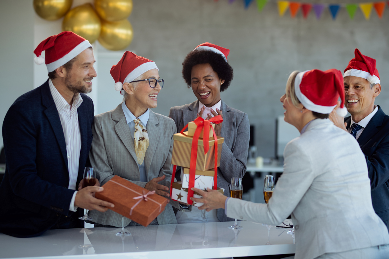 A diverse C-Level Executive Search Firm celebrates the Holidays in the office wearing Santa hats and sharing gifts.